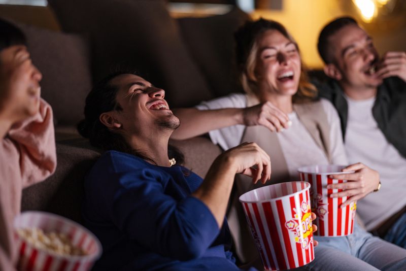 A group of friends laugh and enjoy popcorn during a fun movie night at home, conveying relaxation and joy.