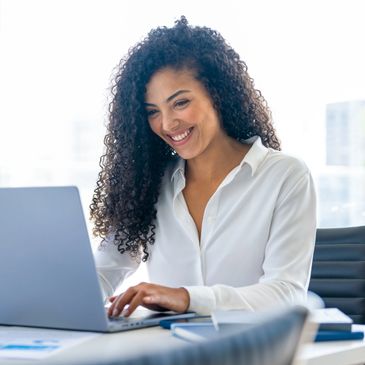 A female professional smiling sitting at a desk with a laptop  