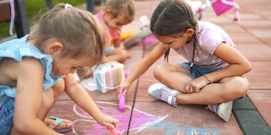Kids drawing colorful chalk art on pavement.