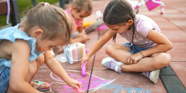 Children drawing with chalk on pavement outside.