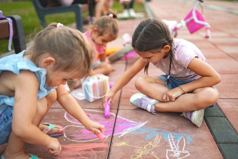 A group of children engaged in creative chalk drawing on a pavement in the park. Laughter fills the air as they express their artistic talents on a bright sunny afternoon.
