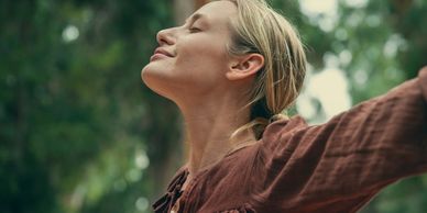 Woman enjoying nature with eyes closed and arms outstretched.