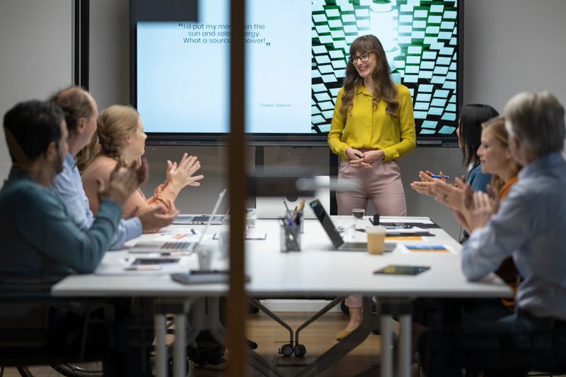 Businessmen and businesswomen clapping hands after successful presentation in conference room.