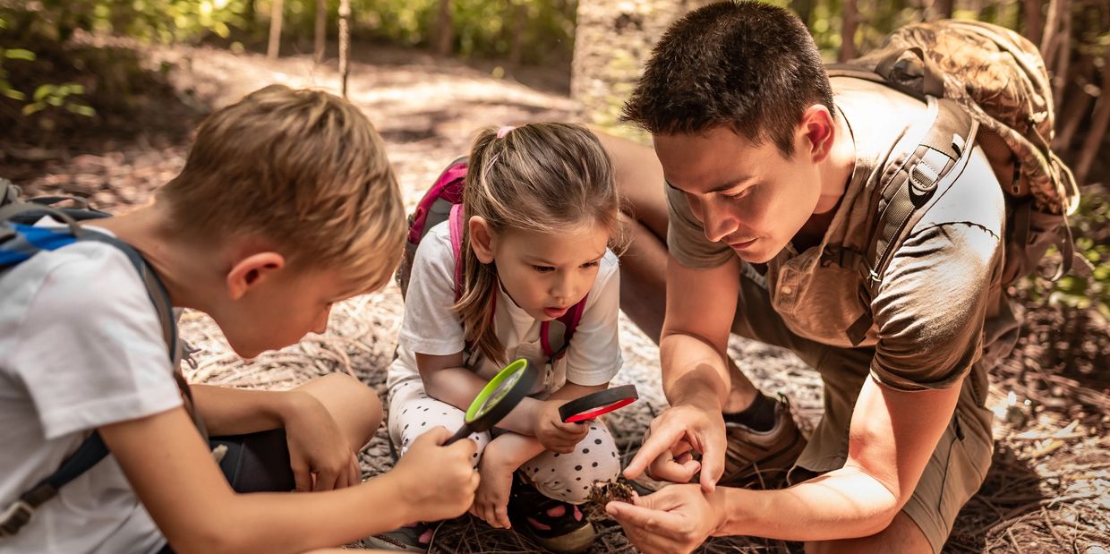 Father and kids exploring nature with magnifying glasses in the forest.