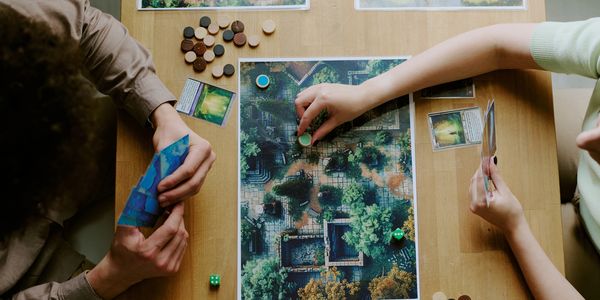 Two people playing a strategic board game with cards and tokens on a wooden table.
