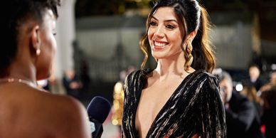 A woman in a black dress smiling during an interview at a formal event.