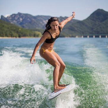 A woman surfing on a lake with mountains in the background.