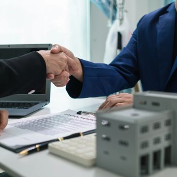 Two professionals shaking hands over a contract in an office setting.