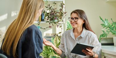 A woman with glasses happily consulting another woman using a tablet.