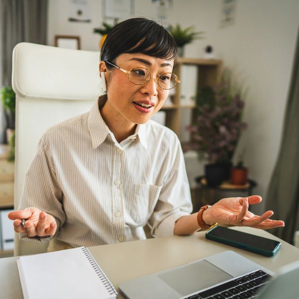Woman with glasses and earbuds engaging in a video call at her desk.