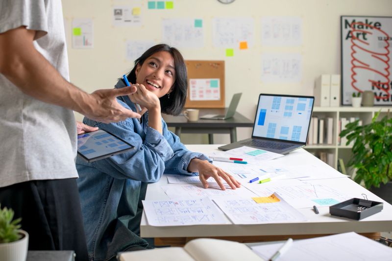 UX/UI designers discussing and brainstorming on wireframes for a website and mobile app prototype, surrounded by sketches of user flow and design tools, in the concept of website and mobile application design concept.