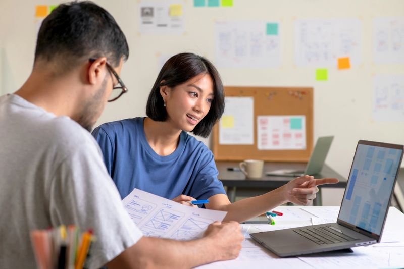 UX/UI designers discussing and brainstorming on wireframes for a website and mobile app prototype, surrounded by sketches of user flow and design tools, in the concept of website and mobile application design concept.