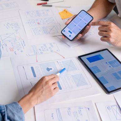 People working on app wireframe designs with phone, tablet, and sketches.