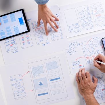 People designing mobile app wireframes with sketches, tablet, and phone.