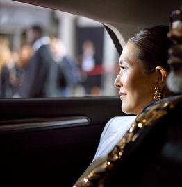 A woman gazes thoughtfully out of a car window in a dimly lit setting.