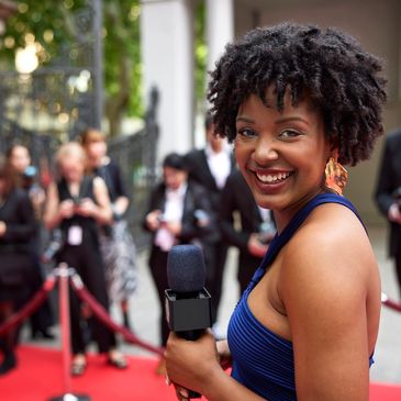 Smiling reporter on red carpet with microphone.