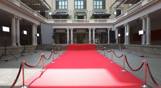 Empty red carpet setup with ropes and lighting in a grand building.