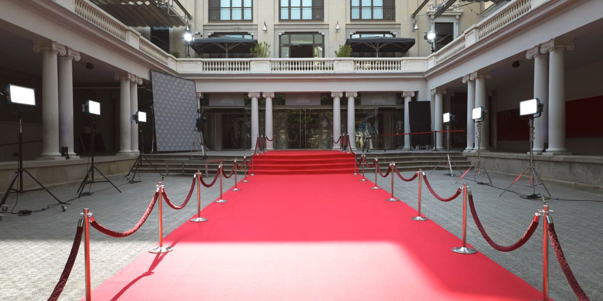 Empty red carpet setup with ropes and lighting in a grand building.