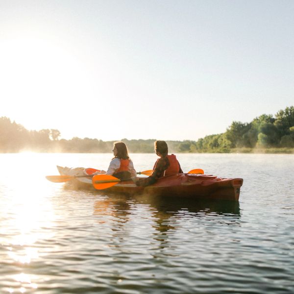 Two people kayaking on a calm lake at sunrise.