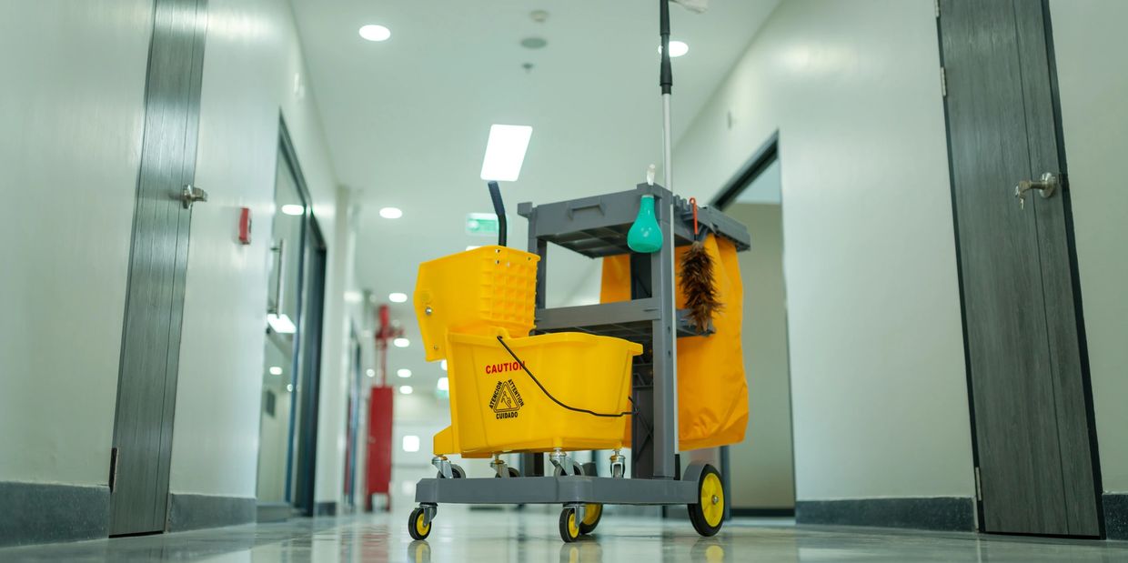 A yellow cleaning cart with caution signs stands in a bright hallway.