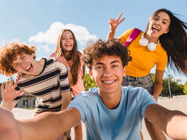 Four cheerful teenagers taking a selfie outdoors on a sunny day.