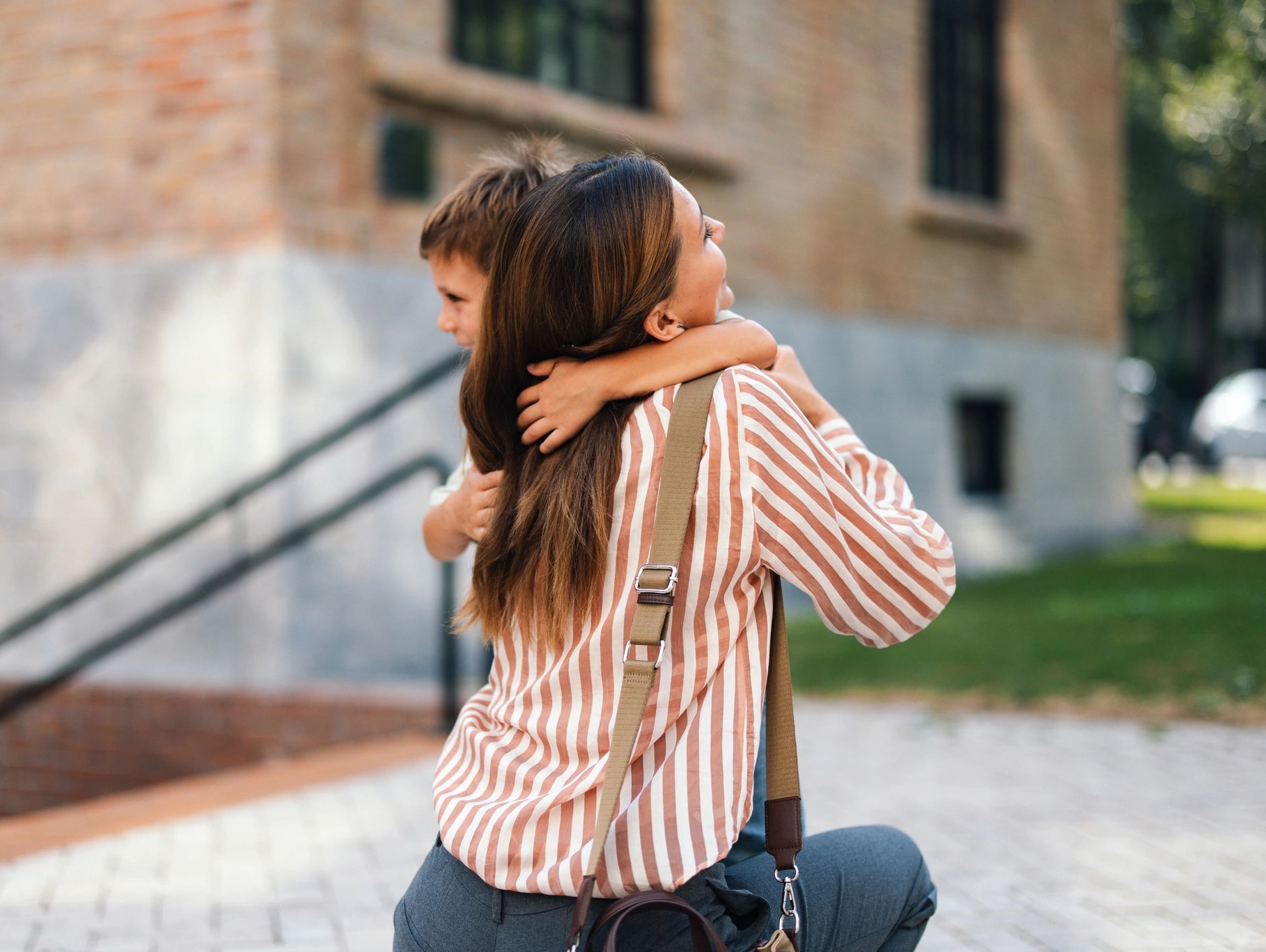 A child joyfully hugs a woman in a warm embrace outdoors.