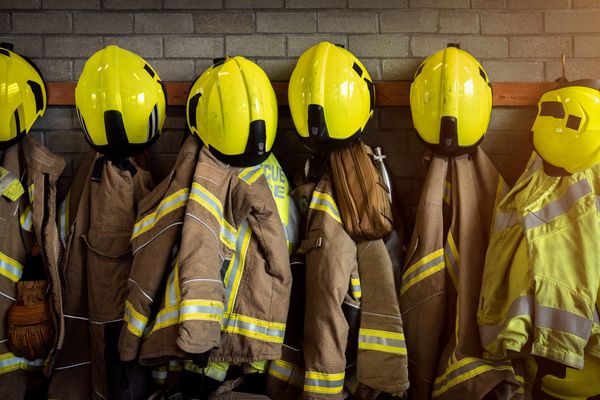 Yellow firefighter helmets and jackets hanging on hooks against a brick wall.