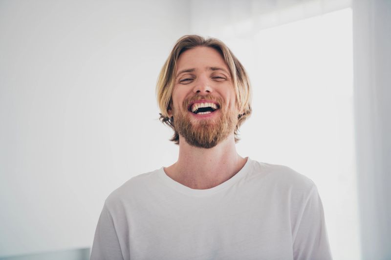 Photo of attractive young male toothy cheerful smile laugh dressed sleepwear cozy day light home interior living room.