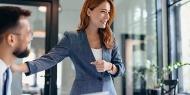Woman in blazer smiling and pointing at a colleague.