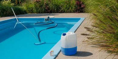 A clean swimming pool with cleaning equipment and chemicals beside it.