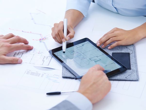 Two people discussing architectural plans using a tablet and printed blueprints.