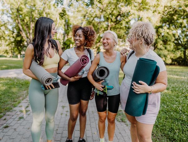 Four women holding yoga mats outdoors, smiling and talking.