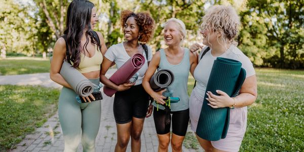 Four women holding yoga mats, walking outdoors and smiling.