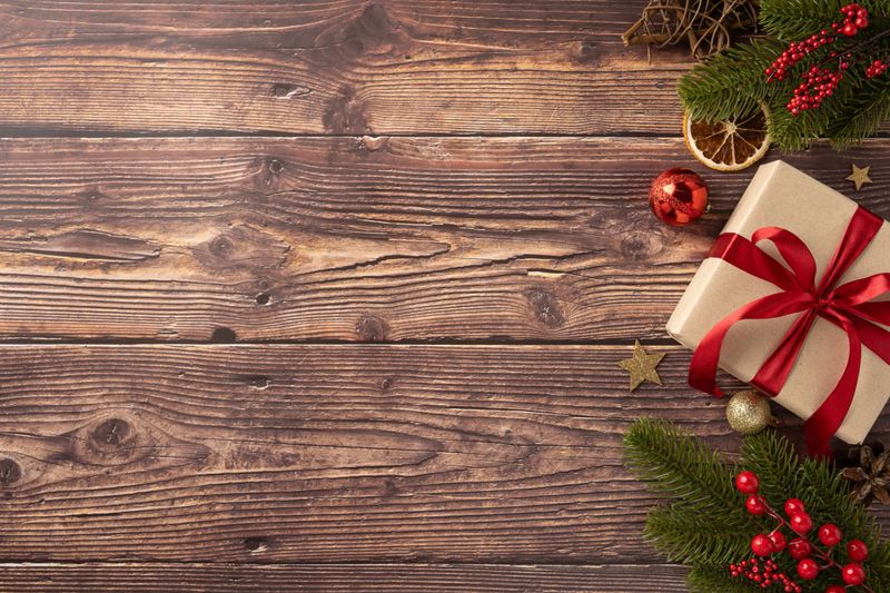 A beautifully wrapped Christmas gift with a red ribbon sits on a wooden table alongside festive decorations, creating a warm holiday atmosphere