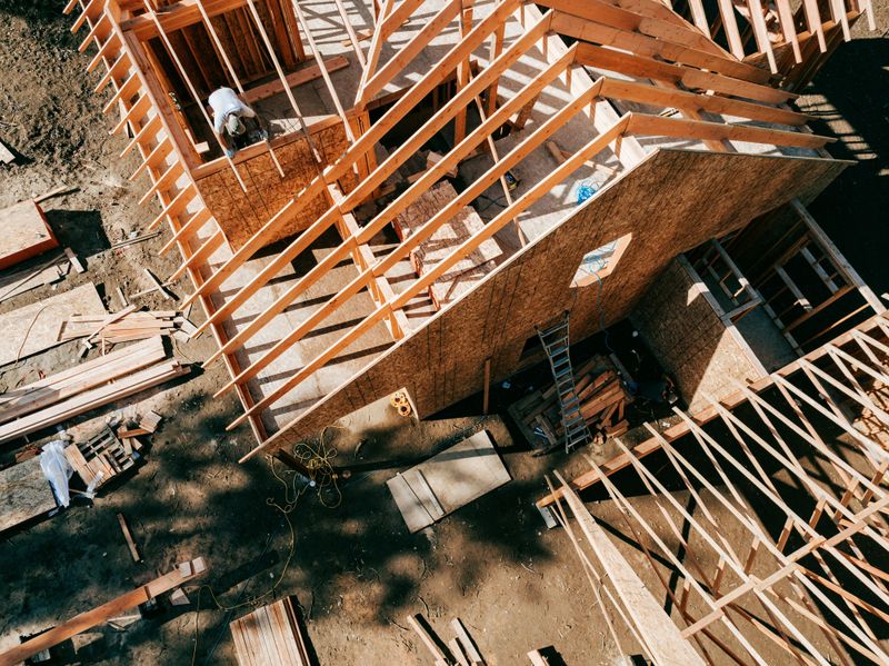 Workers build the frame of a new house project.  Bare plywood and beams as it is framed up from the foundation.  High lumber costs have affected the building process.  Shot in Washington state, USA.