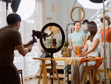 Two women showcasing handbags in a well-lit studio while being filmed.