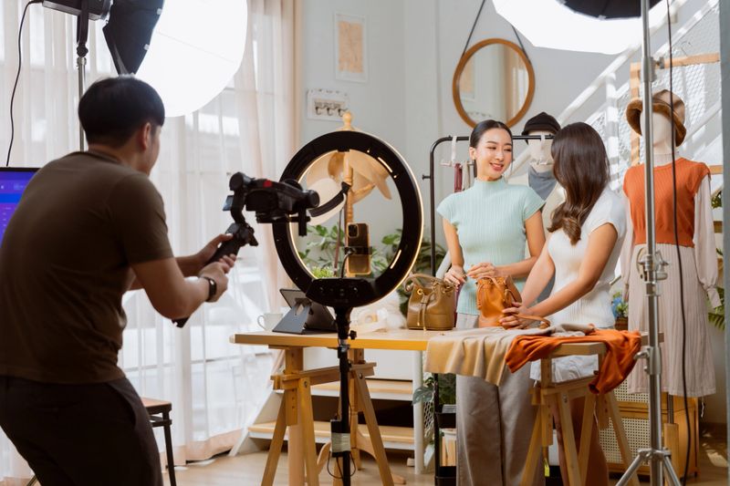 production between home studio full equipment production team and staff Fashion vlogger presenting dress to cellphone and showing clothes selling online live streaming ,Asian small business owner working at home studio, Live video for present clothes