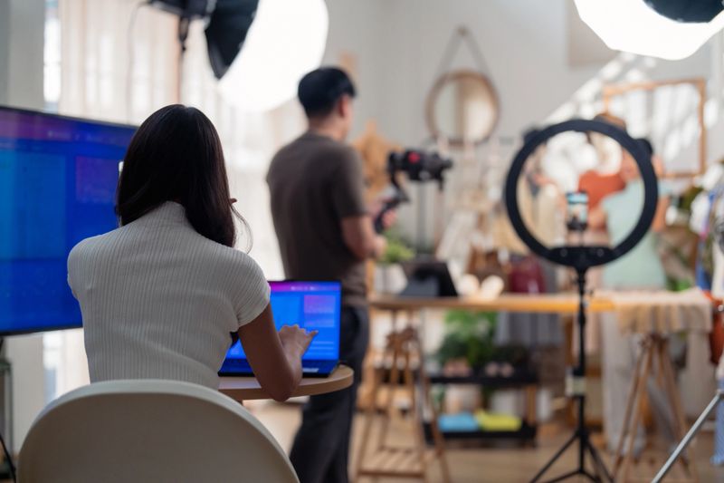 selling live stream online marketing behind back office woman programer checking selling statistic from application screen between stylish influencer woman broadcast selling cloth online SME small business e-commerce