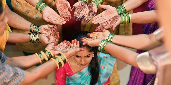 Women with mehndi and bangles surrounding a woman in a traditional ceremony.