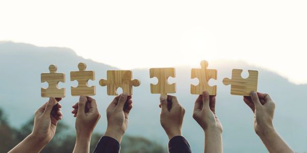 Hands holding wooden puzzle pieces against a bright sky.