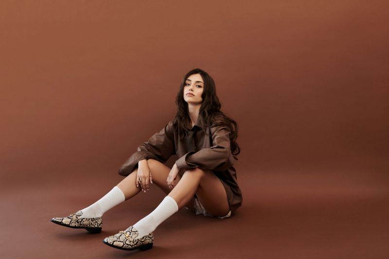 Dressed in autumnal attire, a young woman poses gracefully in a cozy studio, exuding fashion and confidence.