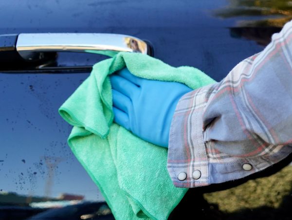 Person wearing blue gloves cleaning a black car door handle with a green cloth.