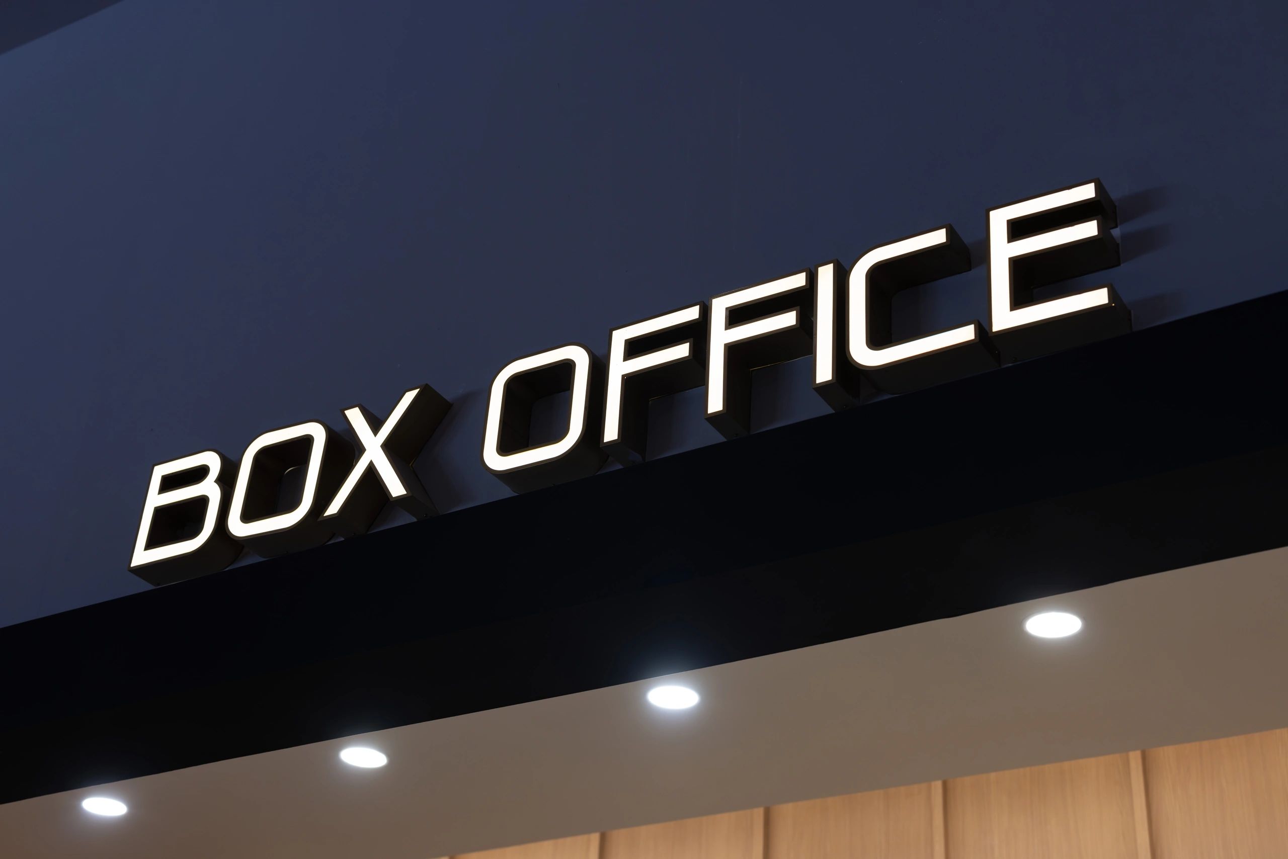 Illuminated BOX OFFICE sign on a dark wall.