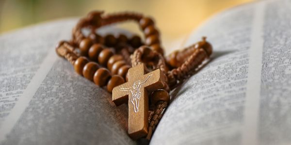 An open bible with a wooden rosary resting on top if it.