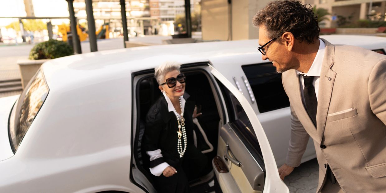 A stylish woman exits a white limousine, greeted by a man in a beige suit.