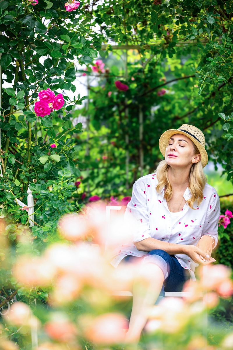 Woman in a garden surrounded by blooming roses, peacefully enjoying the moment