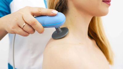 Medical professional using a device on a woman's shoulder for therapy.