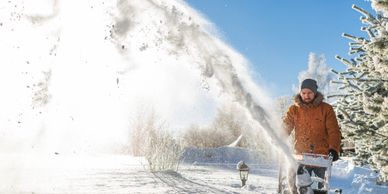 Man clearing snow with a snow blower on a sunny winter day.