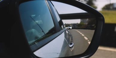 View of a road and cars through a car's side mirror on a sunny day.