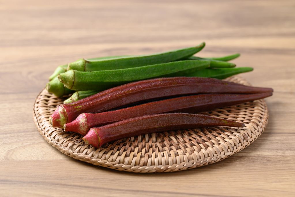 Green and red okra on a woven plate.
